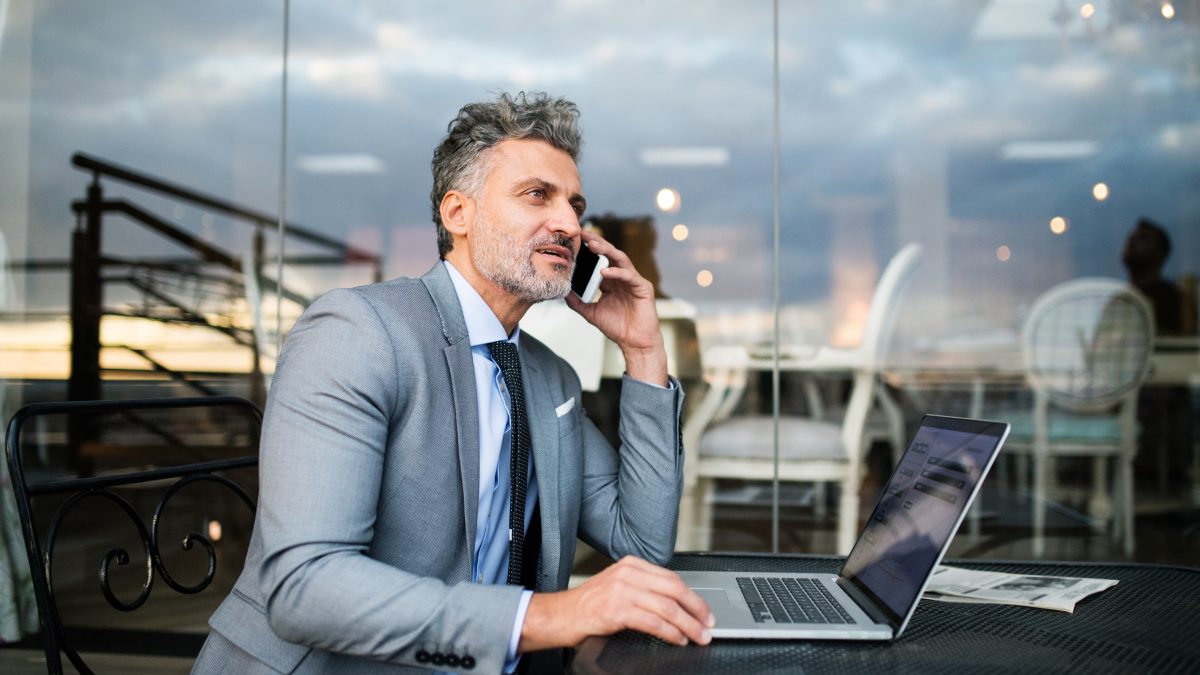 Mature businessman with smartphone in an outdoor hotel cafe.