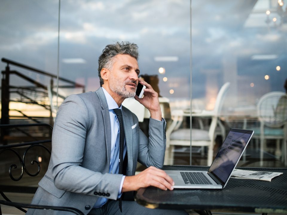 Mature businessman with smartphone in an outdoor hotel cafe.